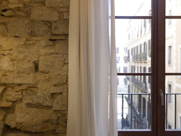 A stone wall adjacent to a window with a view of buildings.