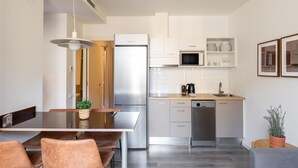A modern kitchen with a stainless steel refrigerator, microwave, and dishwasher. There is a dining area with a table and chairs, and a potted plant on the side. - TWO BEDROOM APARTMENT (Barcelona)