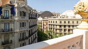 A balcony with ornate balustrades overlooking a cityscape with multi-story buildings.