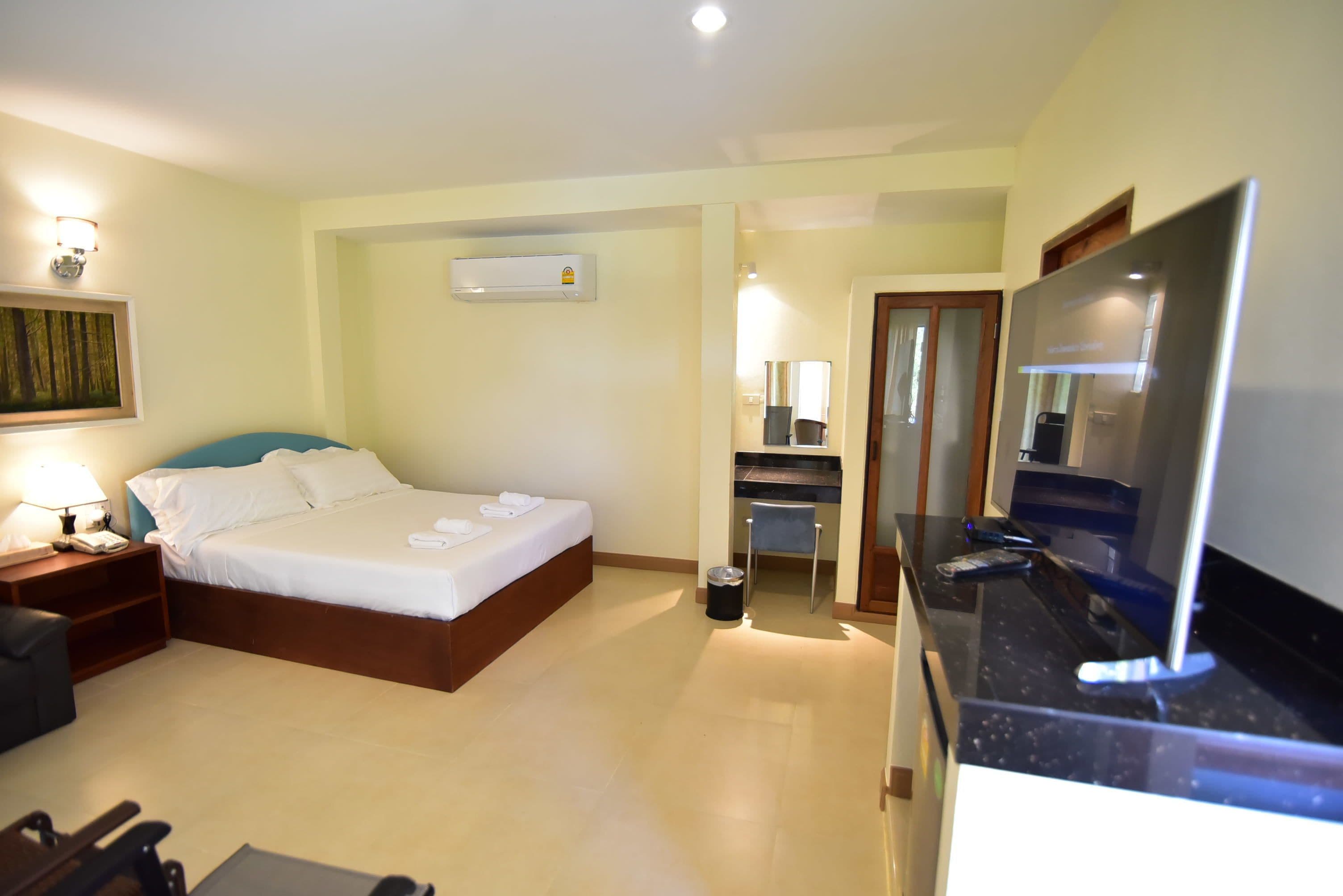 Ein Hotelzimmer mit Bett, Nachttisch, Lampe, Klimaanlage und Fernseher.
