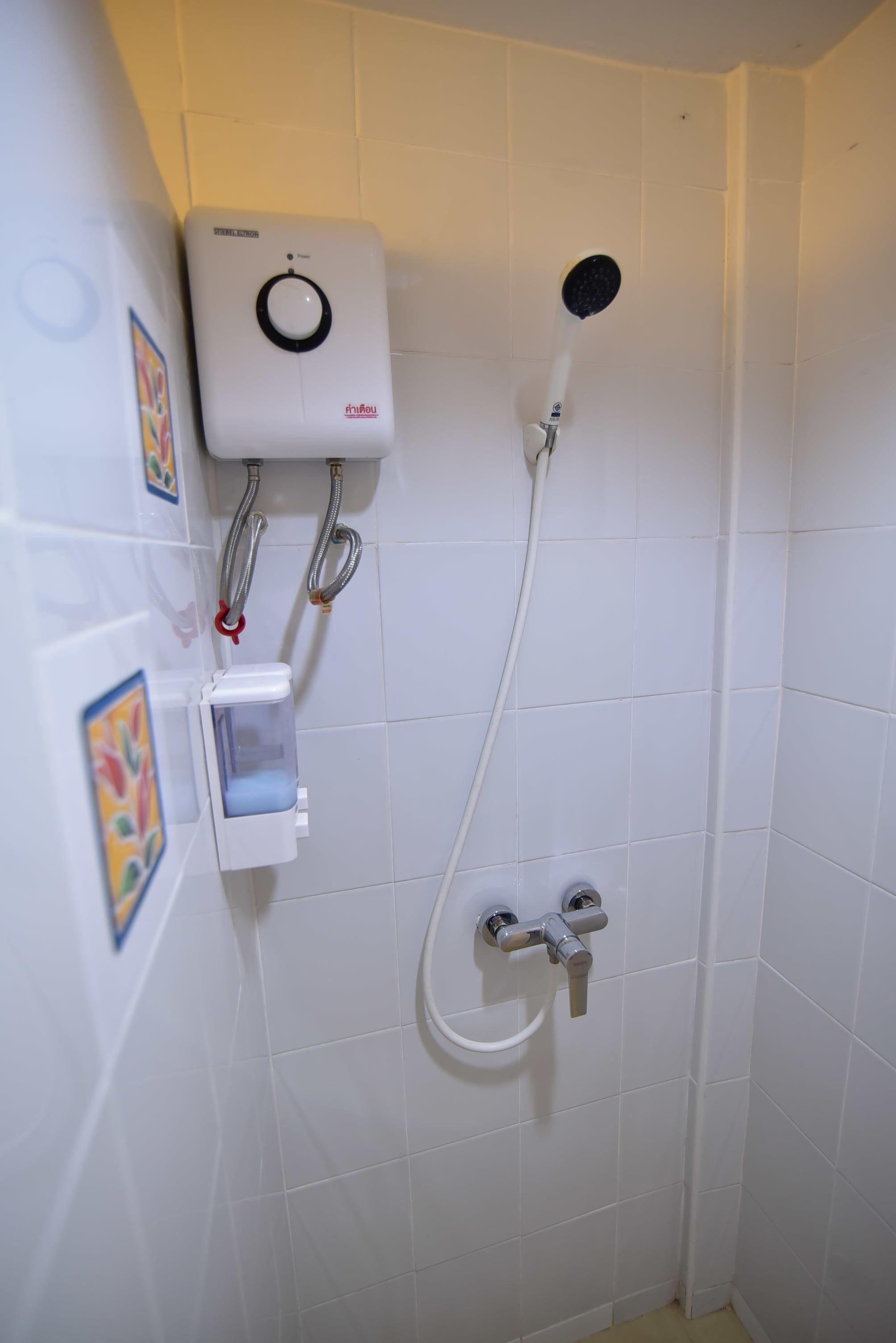 A shower with a control panel, a handheld showerhead, and a wall-mounted faucet.