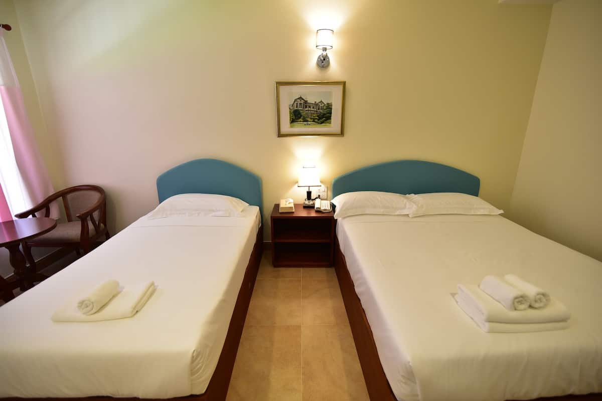 A hotel room with two single beds, a nightstand with a lamp, a framed picture on the wall, and a chair.