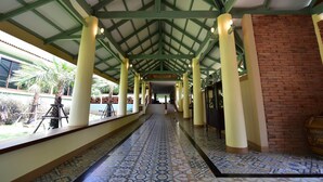 A covered walkway with patterned floor tiles, green structural beams, and a brick wall on one side. - Mamaungpaa Hillside Resort (Takhli)