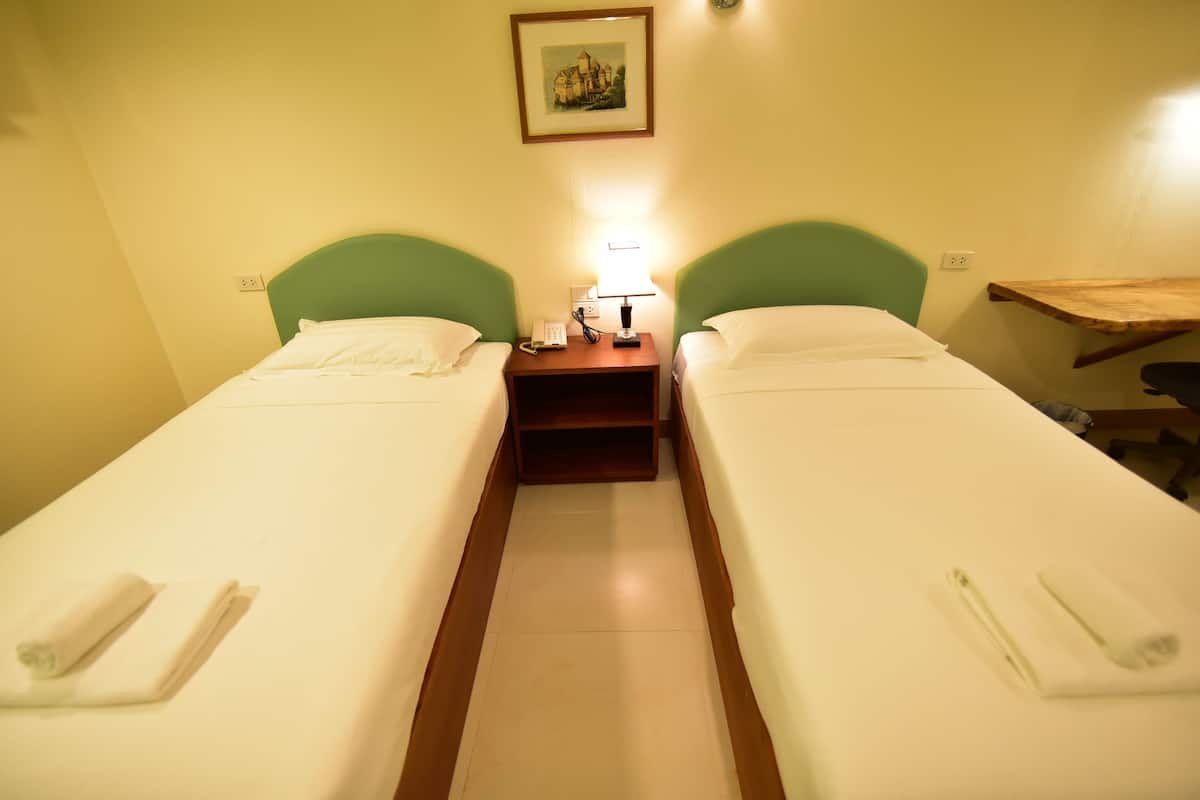 A twin room with two single beds, a bedside table with a lamp, and a small wooden desk.