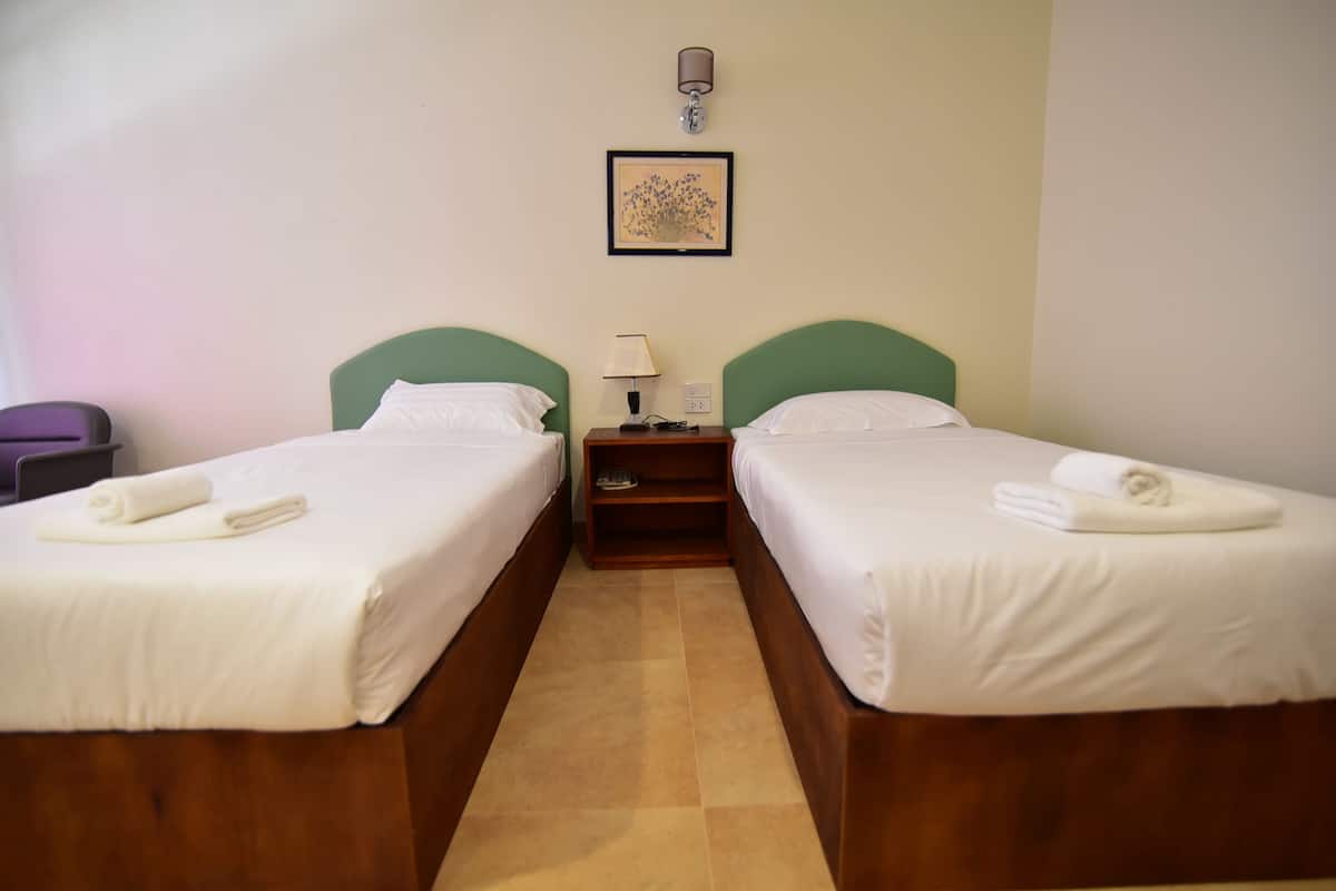 A hotel room with two single beds, a nightstand with a lamp, a framed picture on the wall, and a pair of towels on each bed.