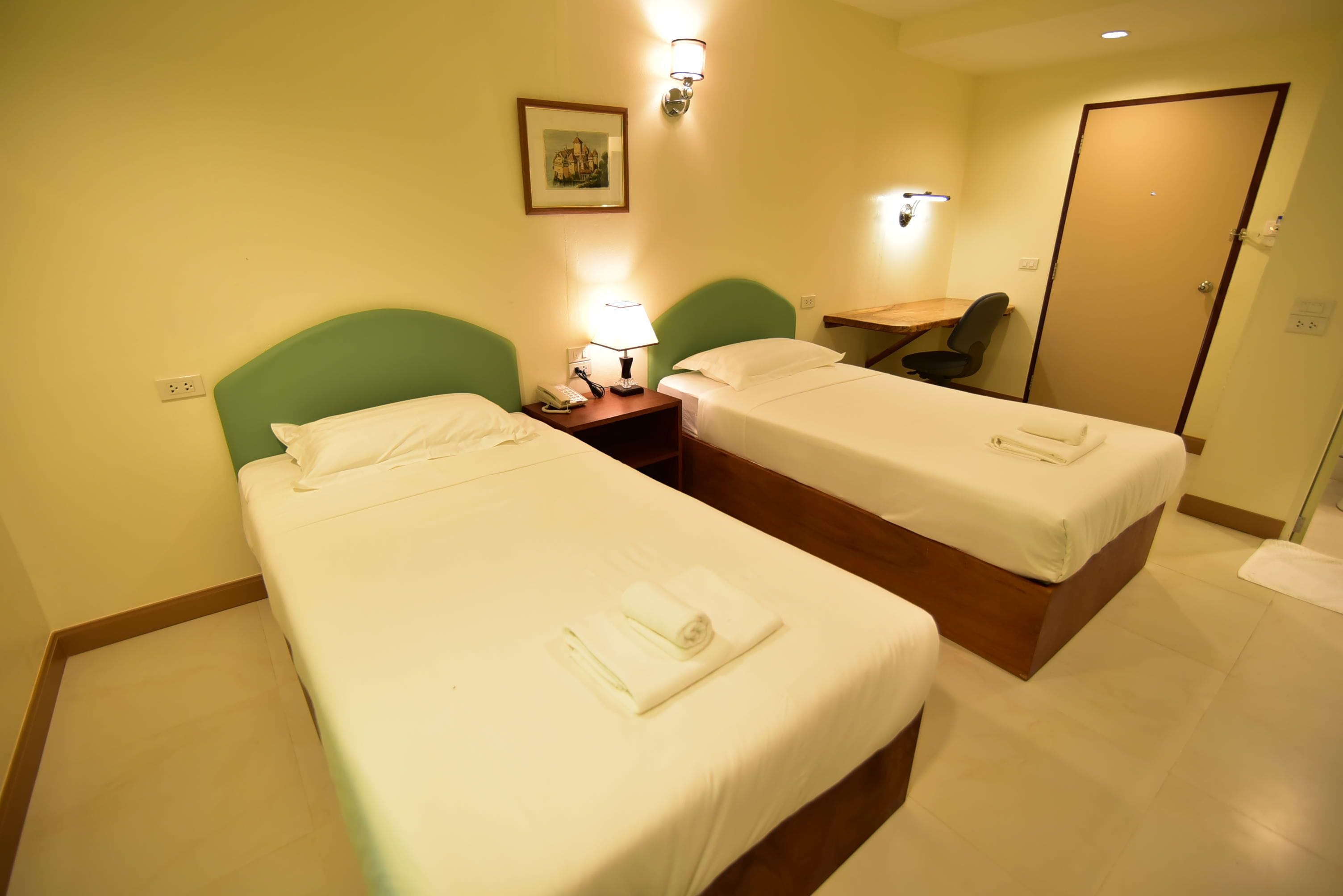 A hotel room with two single beds, a desk, a chair, and a door.
