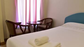 Een hotelkamer met een bed, een ronde tafel, twee stoelen en een raam met gordijnen.