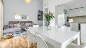 Eine moderne Wohnung mit grauem Sofa, weißem Esstisch und Küchenzeile.