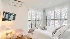 Ein Schlafzimmer mit einem Bett, einem Fernseher, einem Sessel und einem Nachttisch mit Lampe und Blumen.