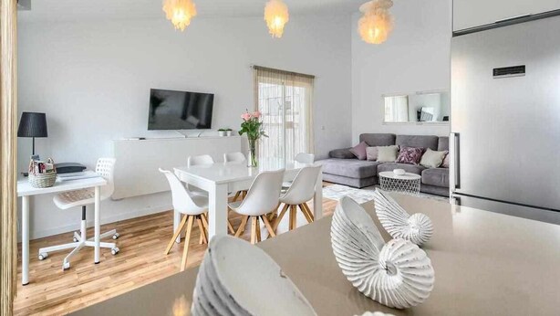 Ein modernes Wohnzimmer mit Essbereich, einem grauen Sofa und einem an der Wand befestigten Flachbildfernseher.
