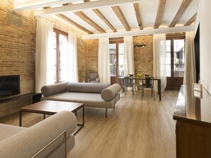 Ein modernes Wohnzimmer mit Sofa, Couchtisch, Fernseher und einem Essbereich mit Tisch und Stühlen.