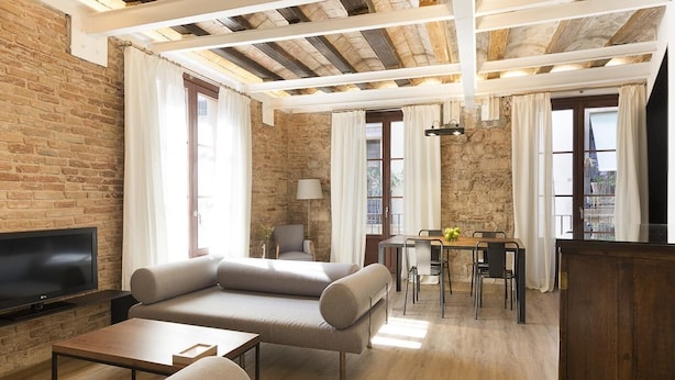 Un salon moderne doté d’un téléviseur à écran plat, d’un canapé, d’une table à manger avec des chaises et d’un mur en pierre.