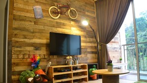 A cozy living area with a wooden wall, a mounted bicycle, a flat-screen TV, and a small table with a plant. - The Woodz Homestay (Tanah Rata)