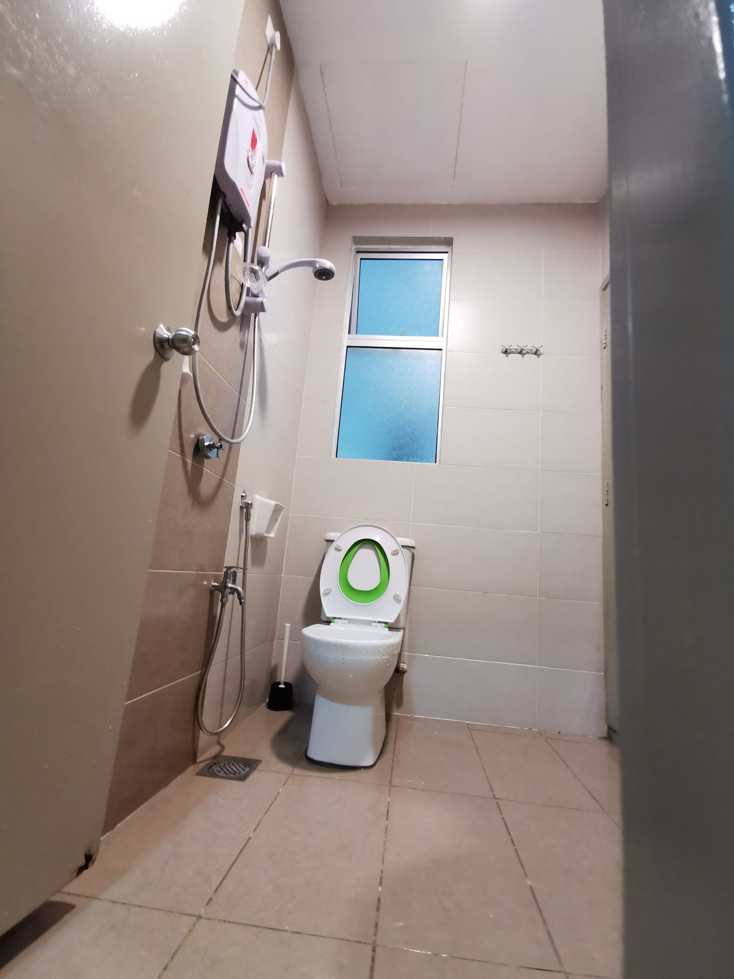 A small bathroom with a toilet, a shower, and a window.