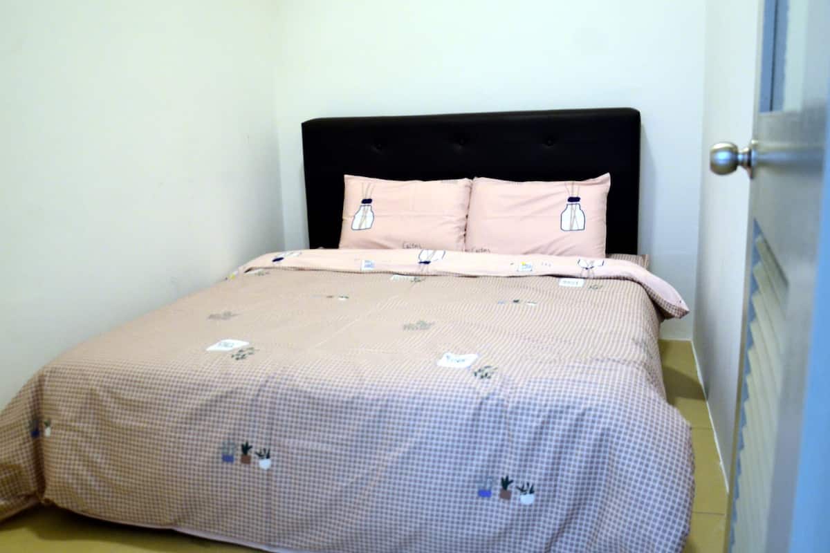 A neatly made bed with a checkered bedspread and two pillows, a black headboard, and a door to the right.