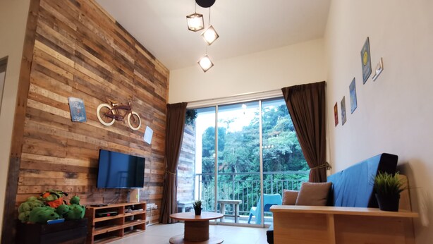 A modern living room with a wooden wall, a TV, a round table, and a sofa. - The Woodz Homestay (Tanah Rata)