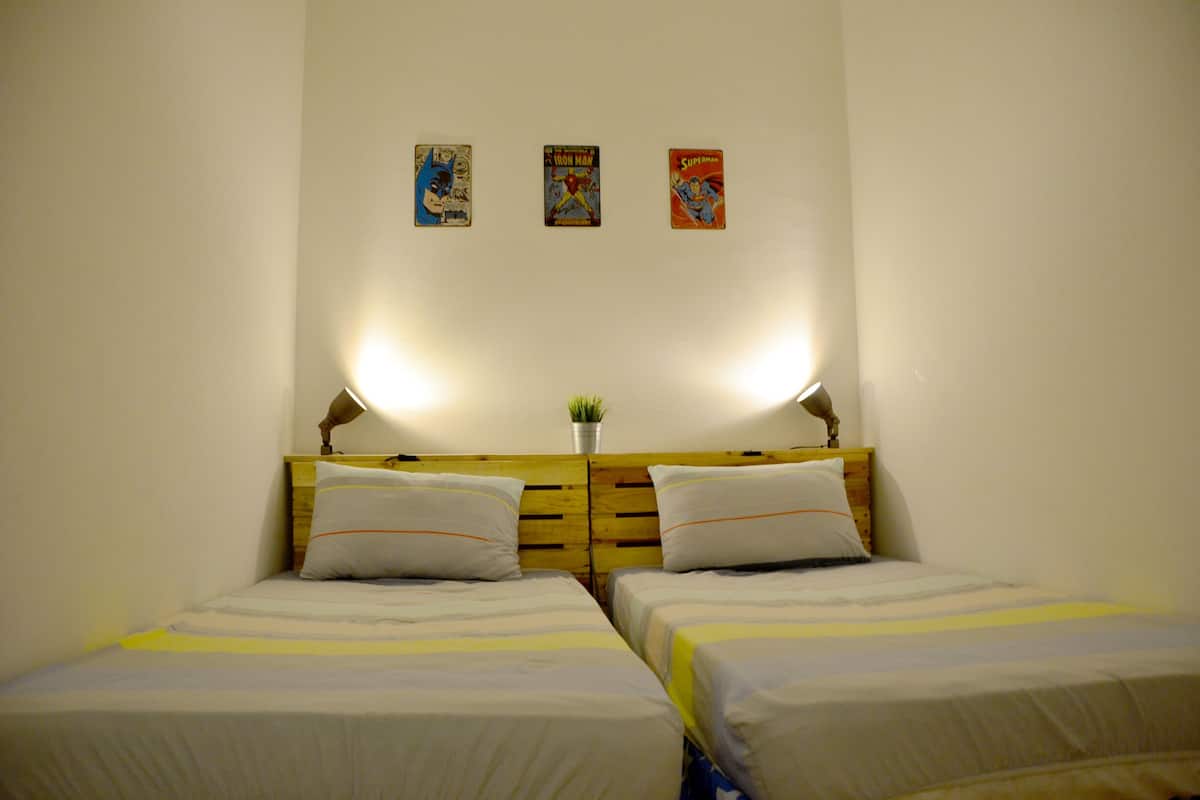 A room with two beds, a wooden headboard, and three comic book posters on the wall.
