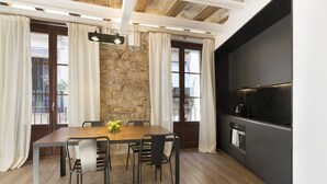 Een eetgedeelte met een houten tafel, zwarte stoelen, een stenen muur en een moderne keuken met donkere kastjes.
