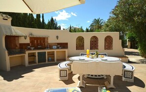 An outdoor kitchen area with a round table and chairs, surrounded by a tiled patio.