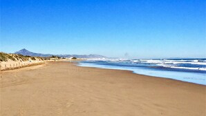 Une vaste plage de sable fin, sous un ciel bleu azur, avec des vagues déferlant sur l’océan.