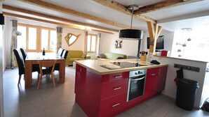 A kitchen with a red island, wooden beams, a dining area with chairs, and a sofa. - Beautifully designed Apartment.  Fully equipped for your holiday needs. Sleeps 7 (Interlaken)