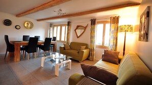 A living room with a wooden ceiling, a sofa, a coffee table, and a dining area with chairs and a table. - Beautifully designed Apartment.  Fully equipped for your holiday needs. Sleeps 7 (Interlaken)