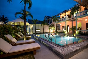 Zona junto a la piscina con sillones de descanso, una alberca y un edificio con balcones.