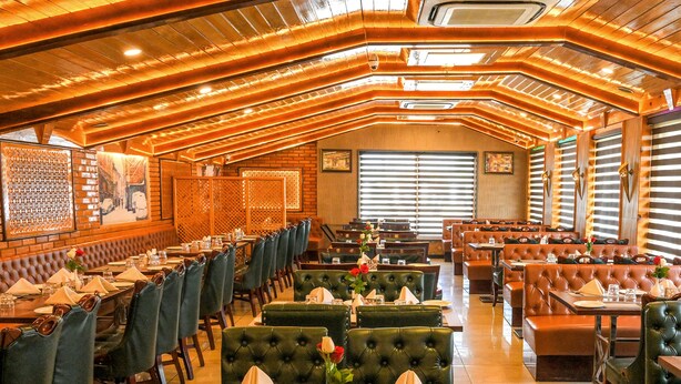 Un restaurante con varias zonas de comedor, incluyendo cabinas y mesas, con un interior cálido de madera y ventanas amplias.