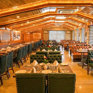 Um restaurante com várias áreas de refeição, incluindo cabines e mesas, com interior em madeira aconchegante e grandes janelas.
