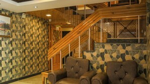 Un vestíbulo con dos sillones de cuero, una escalera con barandillas de madera y paredes de piedra con diseño.