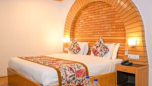 Una habitación de hotel con techo de madera, un arco de ladrillo, una cama con ropa de cama floral, una mesita de noche con una cesta de fruta y una mesita de noche con un teléfono.
