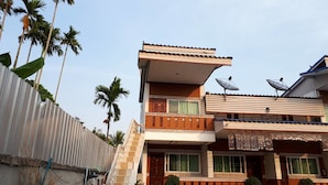 A two-story house with a balcony, satellite dish, and a corrugated metal fence. - Chainam Resort (Chaloem Phra Kiat)
