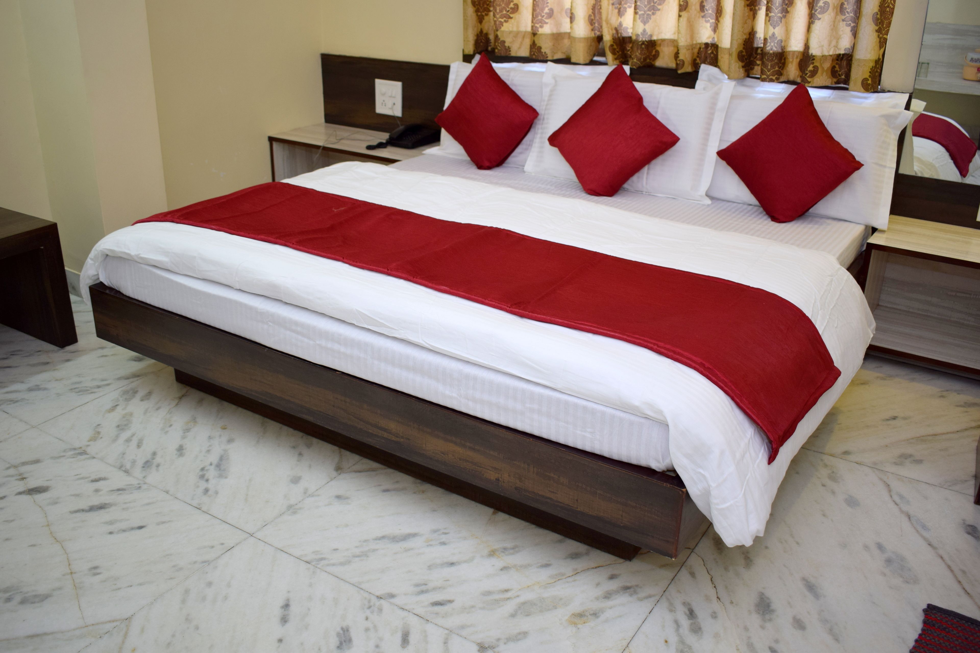 A large bed with a wooden frame, white bedding, and red pillows.