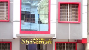 Un hotel llamado "Shivanash" con una fachada moderna, ventanas de marco rojo y una entrada visible.