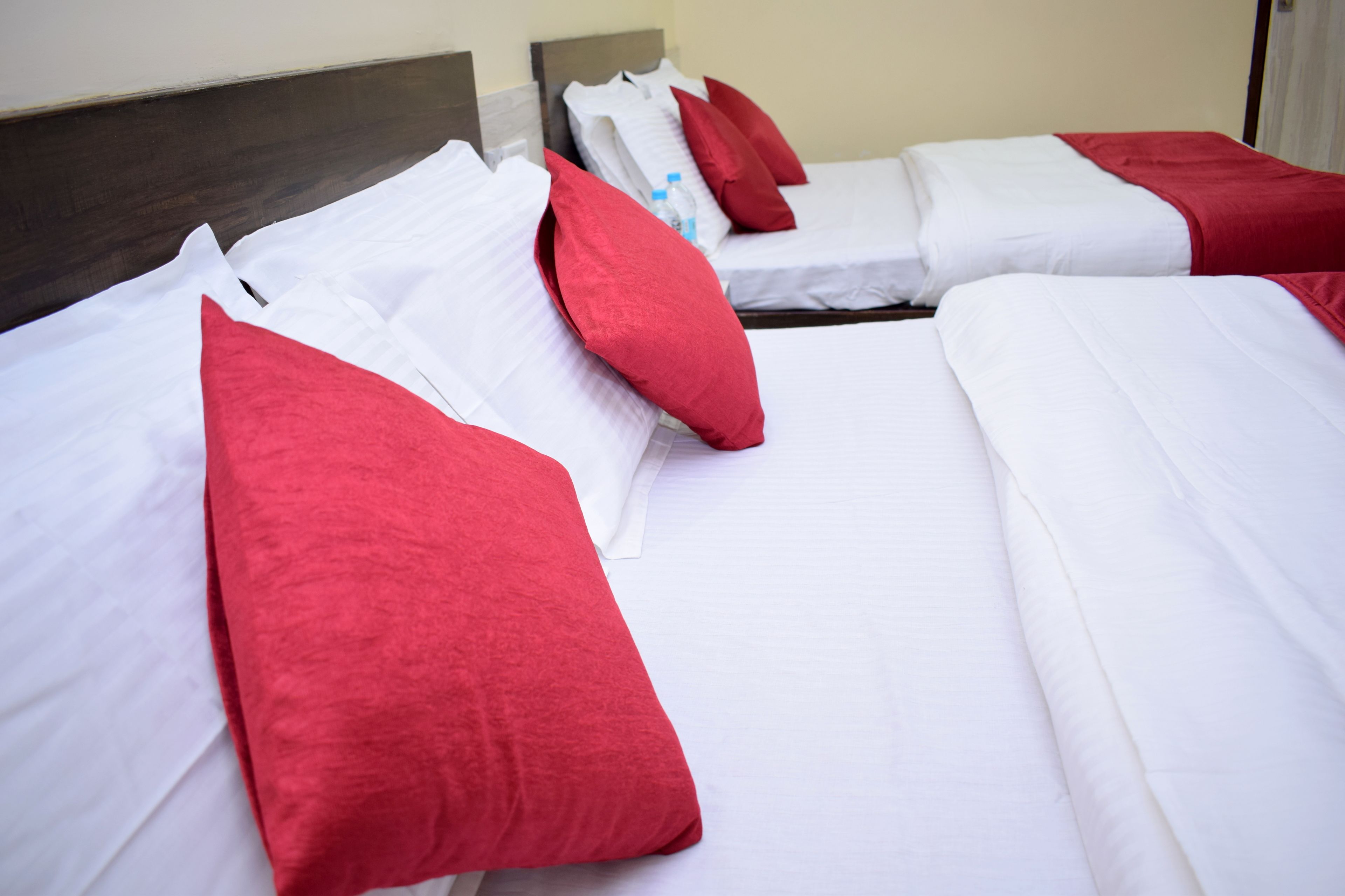 A hotel room with two beds, each with white bedding and red pillows.
