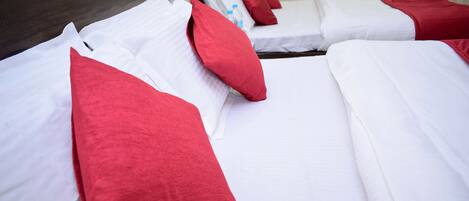 A hotel room with two beds, each with white bedding and red pillows.