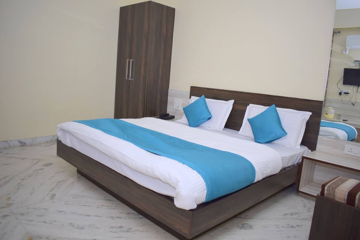 Un letto rifatto con cura, coperto da una trapunta blu e bianca, con una testiera in legno e un comodino con una lampada.