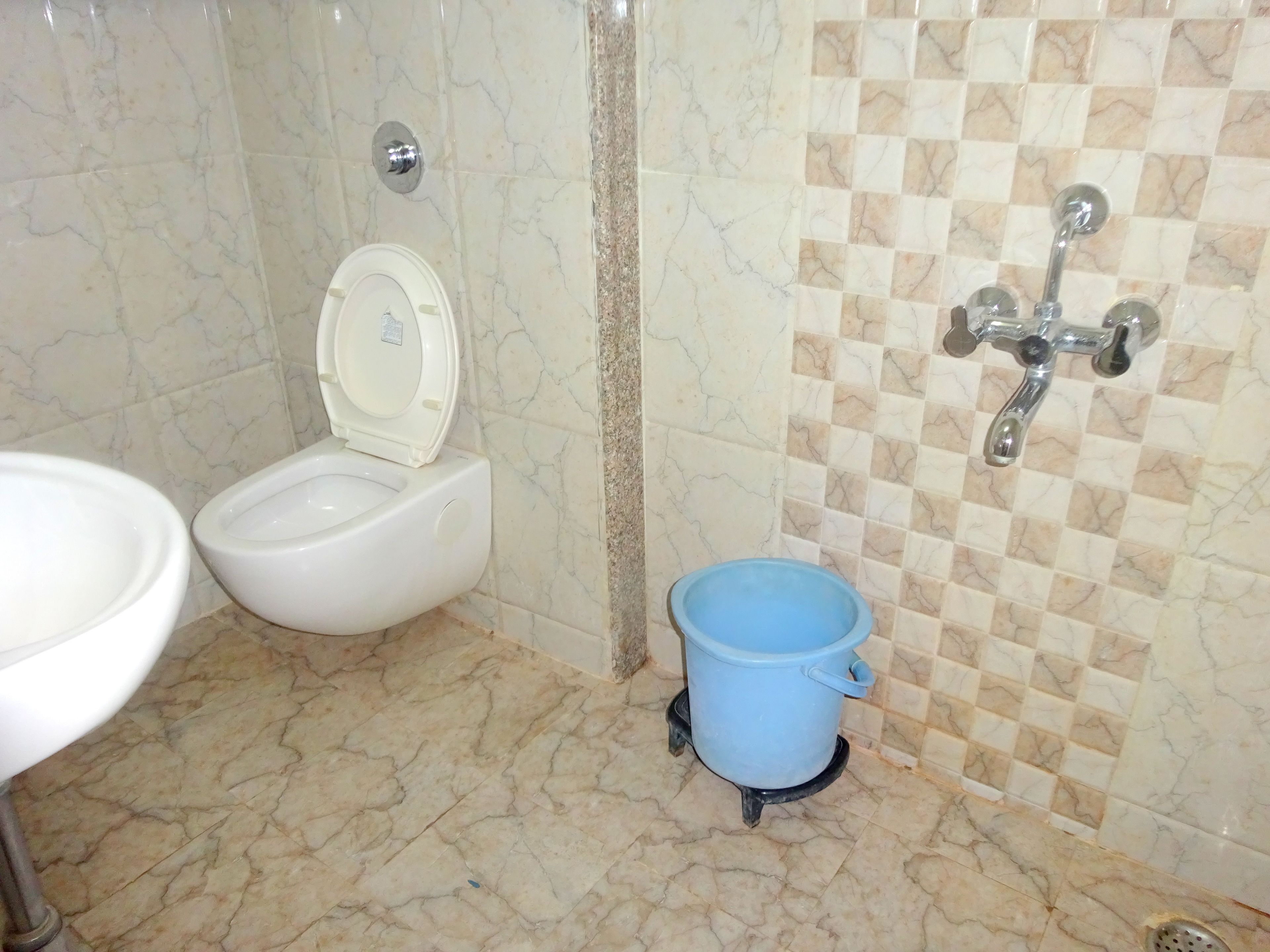 A bathroom with a toilet, bidet, sink, and a blue bucket.