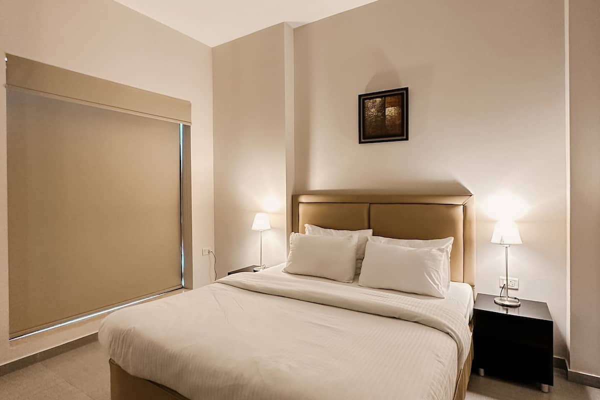 A hotel room with a large bed, two bedside tables with lamps, a headboard, a framed picture on the wall, and a ceiling light.