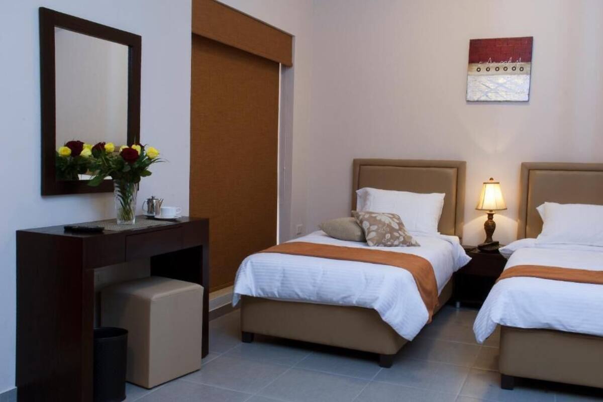 A hotel room with two beds, a desk with a vase of flowers, a mirror, and a wall art piece.