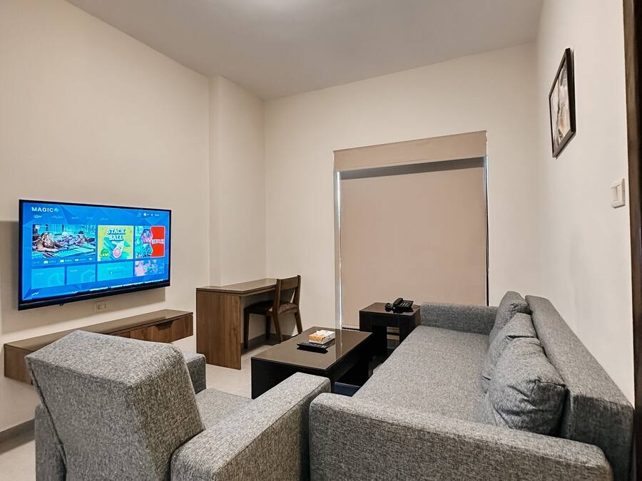 A modern living room with a flat-screen TV, grey upholstered sofa, a wooden coffee table, and a small wooden desk.