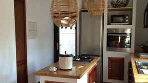 Une cuisine compacte dotée d’un îlot central, de deux lustres suspendus en osier, d’un four à micro-ondes, d’un four traditionnel et d’un évier.