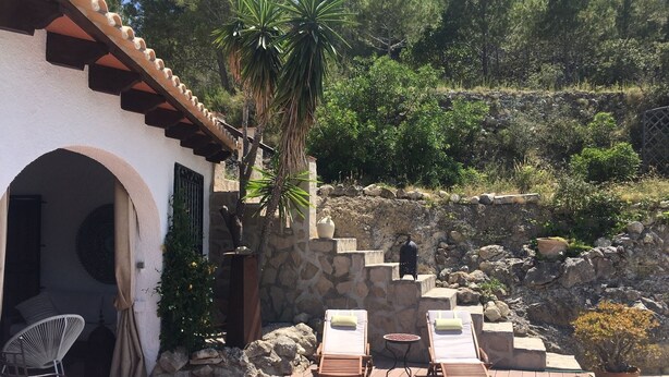 Une terrasse avec des chaises longues, un mur en pierre et un escalier menant au sommet d’une colline.