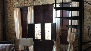 Un intérieur rustique avec des murs en pierre, une porte en bois, un escalier en colimaçon et des meubles à motifs.