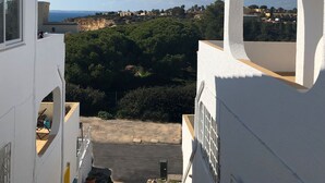 A view from a white building with a window, overlooking a coastal area with greenery and buildings in the distance. - Modern, quietly located vacation apartment with sea view + close to the beach, fully air-conditioned (Carvoeiro (Vale Centeanes))