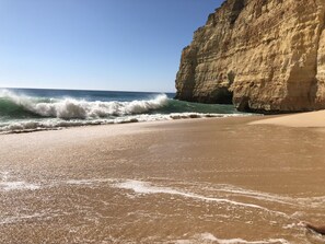 A beach with waves crashing onto the shore, a sandy beach, and a large cliff. - Modern, quietly located vacation apartment with sea view + close to the beach, fully air-conditioned (Carvoeiro (Vale Centeanes))