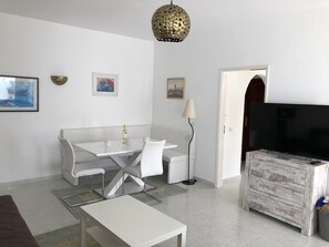 A modern living room with a white sofa, a dining table with chairs, a TV, and a decorative lamp.