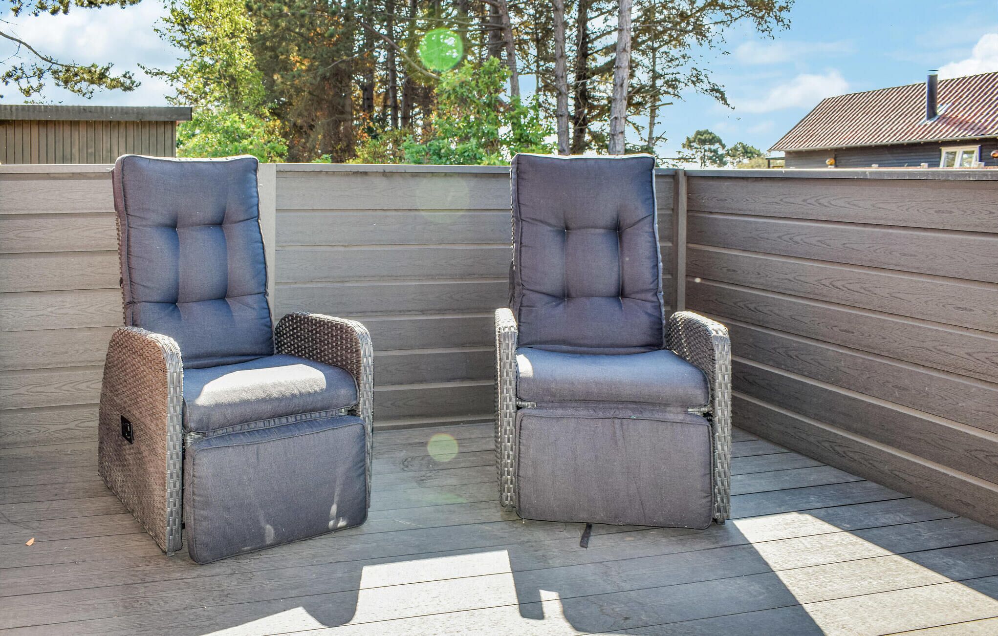 Two grey cushioned chairs with woven bases on a wooden deck.