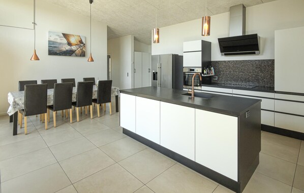 A modern kitchen with a central island, pendant lights, a dining area with chairs, and a kitchen island with a sink.