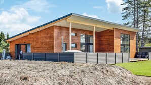 Une cabane moderne en bois, dotée d’un patio couvert, de grandes fenêtres et d’une pelouse bien entretenue.